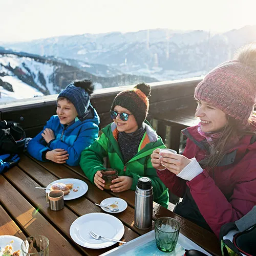 a woman and two children eating food and smiling at a ski lodge